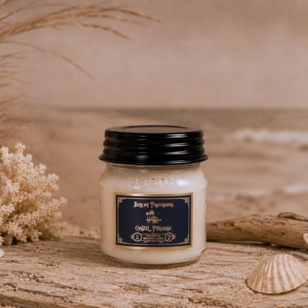Jar candle with a black lid on a wooden surface with dried flowers and a shell.