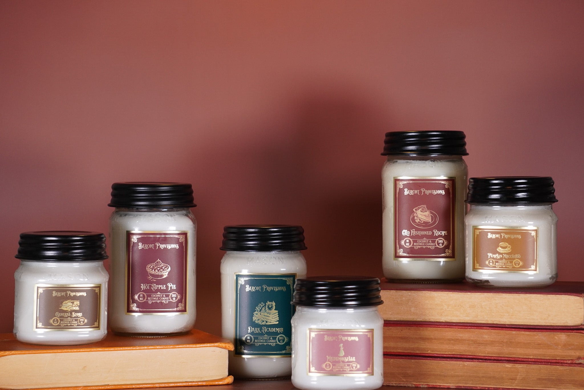 Collection of candles with visible branding on a wooden surface against a red-brown background