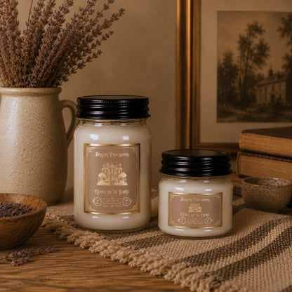Two candles with labels on a rustic surface with decorative elements.