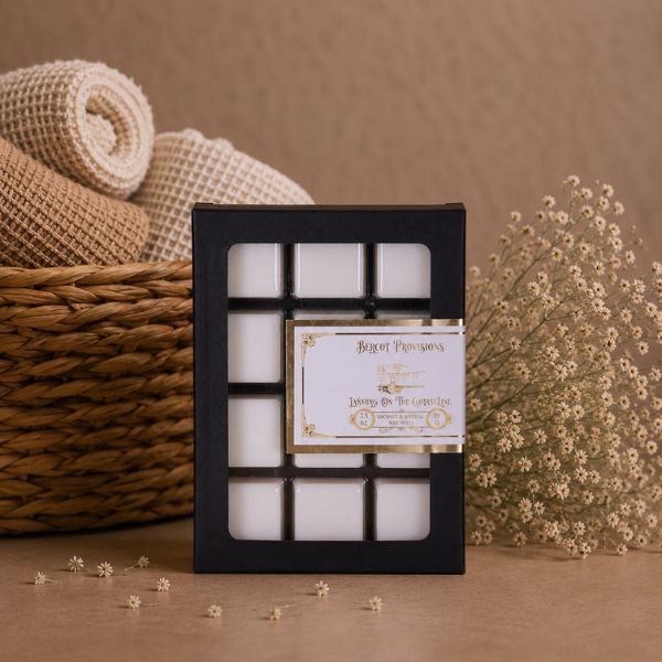 Set of white cubes of scented wax melts in a black box with a decorative label, placed on a brown surface with a woven basket and flowers in the background.
