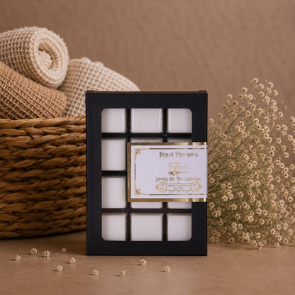 Set of white cubes of scented wax melts in a black box with a decorative label, placed on a brown surface with a woven basket and flowers in the background.